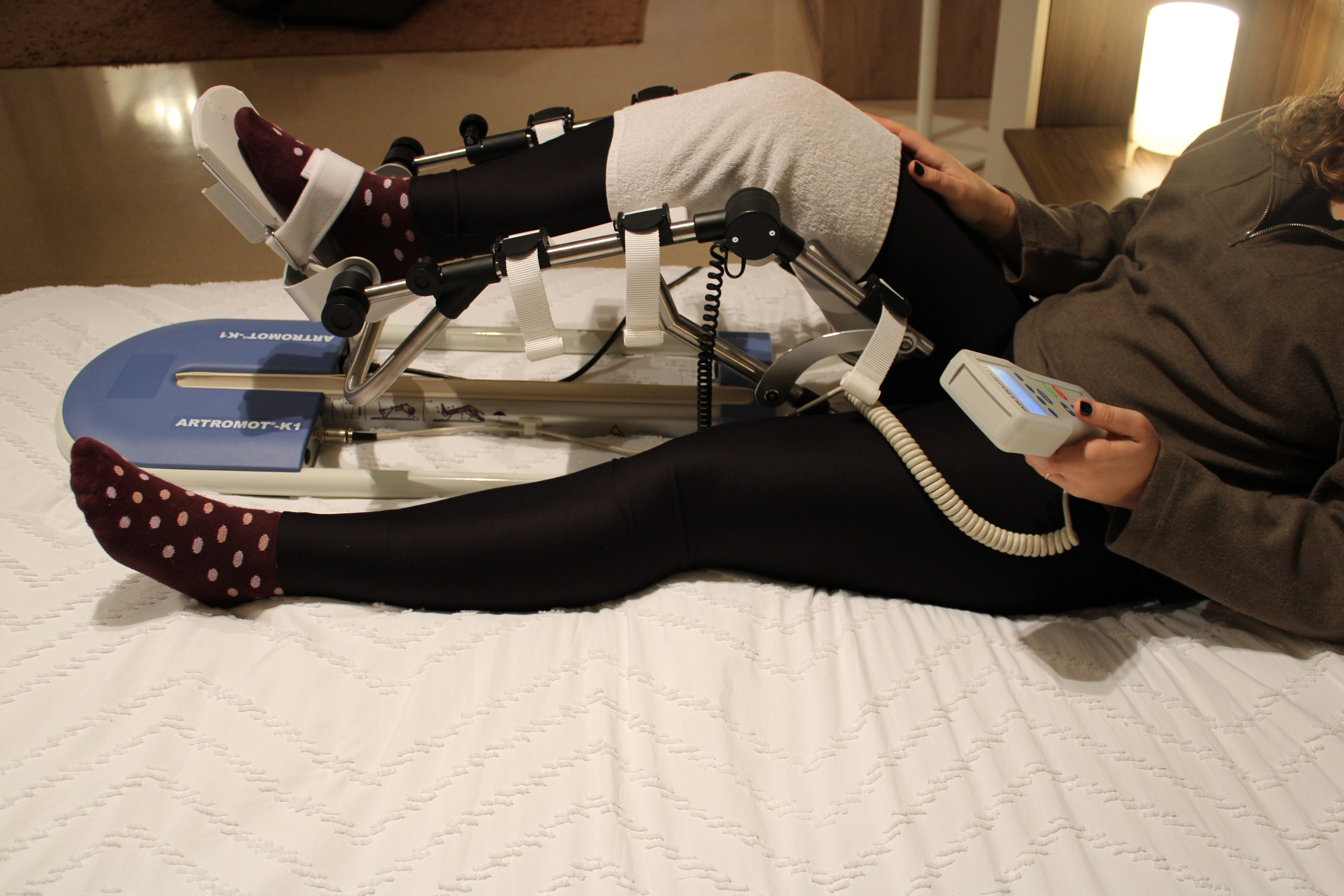 Artromotor k1 en cama colocado en pierna derecha con mando en la mano